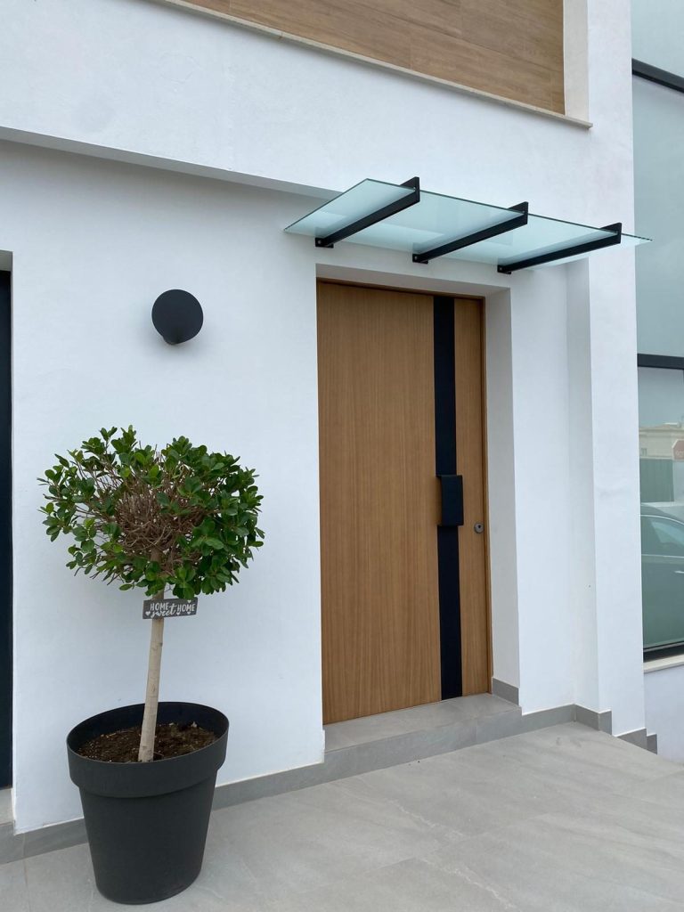 Puerta de madera con un toldo de cristal y una planta en una maceta junto a la entrada.