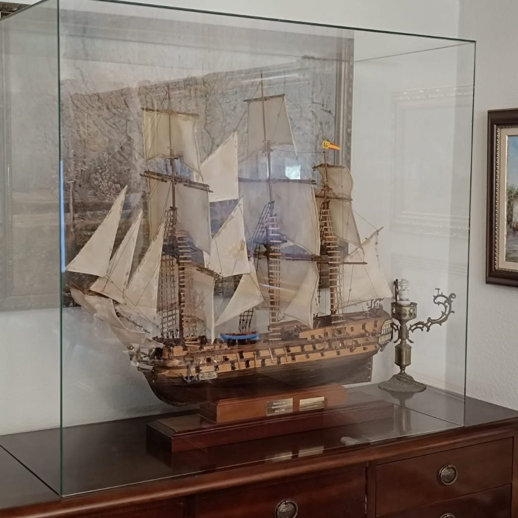 Maqueta de barco antiguo en vitrina, con velas blancas y detalles de madera.